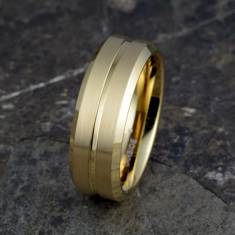 Gold tungsten 8mm mens wedding band tilted showing CARBIDE engraving inside and brushed bands separated by polished groove, comfort fit ring on stone