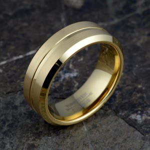 Gold tungsten carbide 8mm ring angled showing brushed matte bands with polished offset groove, TUNGSTEN CARBIDE engraved interior, mens wedding band