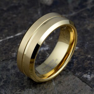 Gold tungsten 8mm mens band angled displaying brushed texture flanking polished center groove, TUNGSTEN CARBIDE interior stamping, wedding ring on stone