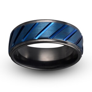 May include: A black and blue patterned ring with a brushed finish. The ring has a wide band with a black outer edge and a blue center with diagonal lines.