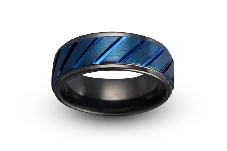May include: A black and blue patterned ring with a brushed finish. The ring has a wide band with a black outer edge and a blue center with diagonal lines.