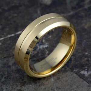 Gold tungsten carbide 8mm ring tilted showing brushed matte finish with polished groove accent and TUNGSTEN CARBIDE engraving inside, mens wedding band