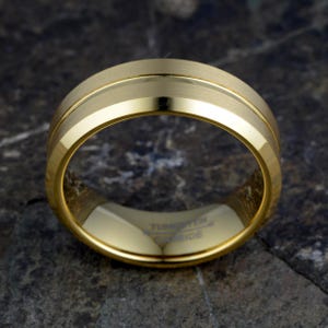 Gold tungsten 8mm ring flat displaying TUNGSTEN CARBIDE interior engraving and brushed exterior with polished offset groove, mens band horizontal on concrete