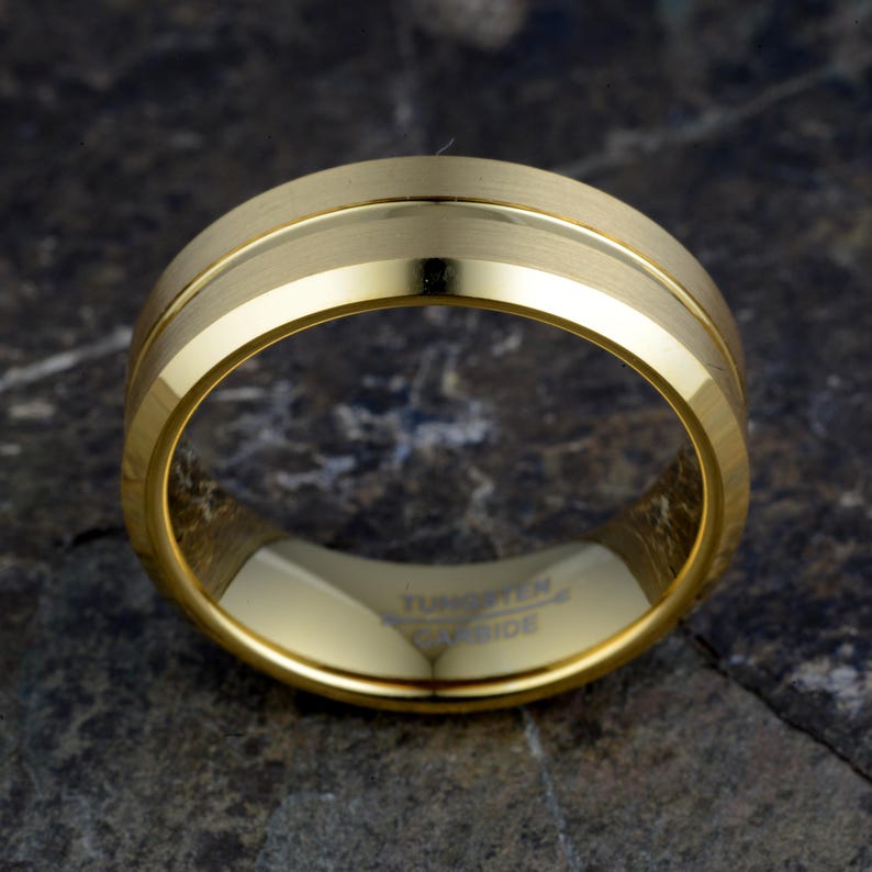Gold tungsten 8mm ring flat displaying TUNGSTEN CARBIDE interior engraving and brushed exterior with polished offset groove, mens band horizontal on concrete