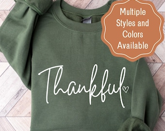 May include: A green sweatshirt with the word "Thankful" written in white cursive with a small heart next to it. The text is centered on the sweatshirt.