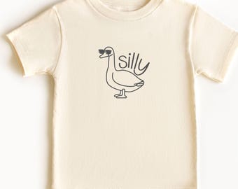 May include: A cream coloured short-sleeved t-shirt with a black line drawing of a goose wearing sunglasses and the word "silly" printed on the front.