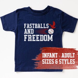 Puede incluir: Camiseta azul marino con las palabras "FASTBALLS AND FREEDOM" en letras blancas. Un águila roja está sobre una pelota de béisbol. Disponible en tallas de bebé y adulto.
