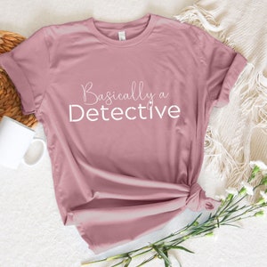 May include: A dusty rose t-shirt with the text "Basically a Detective" in white.