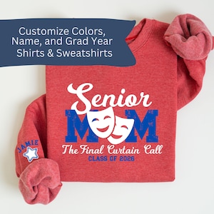 May include: A red sweatshirt with the text "Senior Mom" in white and blue, featuring theater masks. The sleeve displays "JAMIE" and a star. The phrase "The Final Curtain Call CLASS OF 2026" is also visible. The image also includes the text "Customize Colors, Name, and Grad Year Shirts & Sweatshirts."