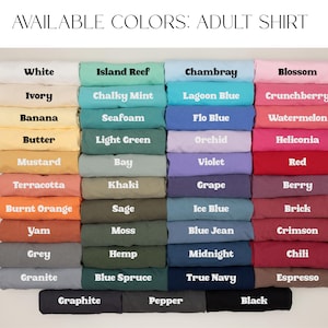 May include: A display of folded adult shirts in various colors, including white, blue, green, and pink. The text "AVAILABLE COLORS: ADULT SHIRT" is at the top, with color names like "White," "Chambray," and "Blossom" displayed on each shirt.