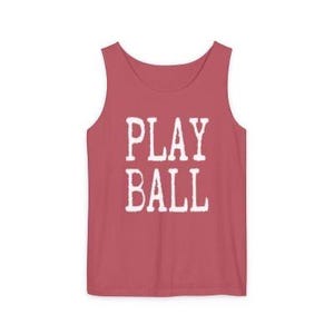 Puede incluir: Una camiseta sin mangas de color rosa polvoriento con el texto PLAY BALL impreso en una fuente blanca desgastada en el centro del pecho. La prenda tiene un cuello redondo y tirantes anchos, ofreciendo un dise&ntilde;o sencillo y limpio.