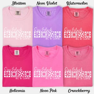 May include: Six t-shirts in various shades of pink, purple, and red. Each shirt has the text "One Block at a time" with a geometric design. Colors include Blossom, Neon Violet, Watermelon, Heliconia, Neon Pink, and Crunchberry.