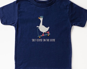 May include: A navy blue t-shirt featuring a white goose wearing sunglasses and a blue hat, riding a scooter. The text "Silly Goose on the Loose" is printed below the goose.