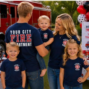 May include: A set of matching navy blue t-shirts for a family, featuring white and red fire department themed graphics. The shirts display text including 'YOUR CITY FIRE DEPARTMENT', 'STATION 1 BROTHER', 'STATION 1 DECLAN', 'STATION 1 MOMMY', and 'STATION 1 SISTER'.