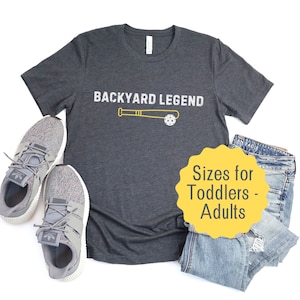 May include: A dark gray t-shirt with the text "Backyard Legend" and a baseball bat and ball graphic. The shirt is available in sizes for toddlers to adults.