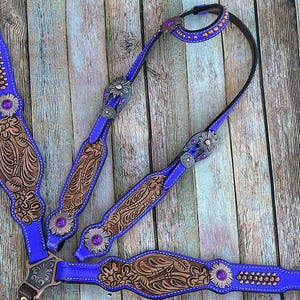May include: Purple leather horse tack set with brown tooled leather accents and purple and silver conchos. The set includes a headstall, breast collar, and reins.