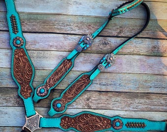 May include: A turquoise leather horse headstall and breast collar set with brown floral tooling and silver accents. The set features turquoise and silver conchos.