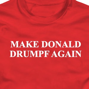 Puede incluir: Camiseta roja con texto blanco que dice "MAKE DONALD DRUMPF AGAIN".