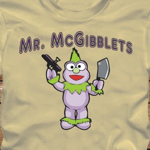 May include: A yellow t-shirt with a purple cartoon character holding a gun and a knife. The text "Mr. McGiblets" is printed on the shirt.