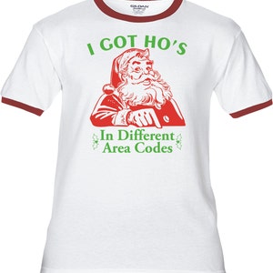 May include: White t-shirt with a red ringer, featuring a cartoon image of Santa Claus pointing to the text "I got ho's in different area codes".