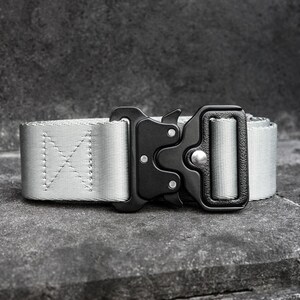 Könnte beinhalten: Ein hellgrauer taktischer Gürtel mit einer schwarzen Metallschnalle. Der Gürtel besteht aus einem strapazierfähigen, gewebten Material und verfügt über einen sicheren Verschluss. Die Schnalle hat ein mattes Finish.