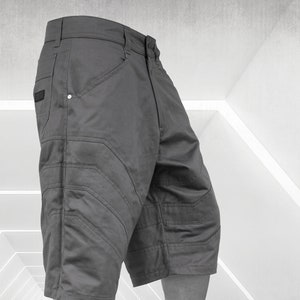 May include: Gray cargo shorts with multiple pockets and stitched detailing. The shorts are paired with black high-top sneakers. The image is set against a bright, geometric background, showcasing urban streetwear.