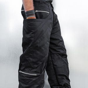 Peut inclure: Pantalon cargo noir avec coutures diagonales et fermetures éclair argentées. Le pantalon comporte plusieurs poches et est associé à des baskets noires. Le style général est moderne et audacieux.