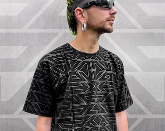 Puede incluir: Una camiseta negra con un patrón geométrico en plata. La camiseta tiene cuello redondo y mangas cortas. El modelo lleva pantalones negros y gafas de sol.
