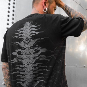 Puede incluir: Camiseta negra con un diseño abstracto gris en la espalda. El diseño se asemeja a una placa de circuito o un patrón futurista.