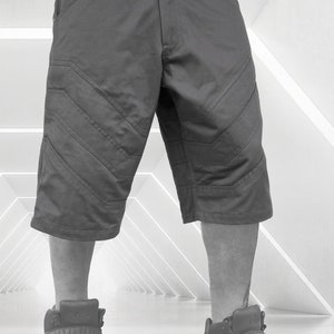 May include: Charcoal gray knee-length shorts with angled stitching details. The shorts have a button closure and pockets. The model is wearing high-top sneakers. The shorts are a modern, casual style.