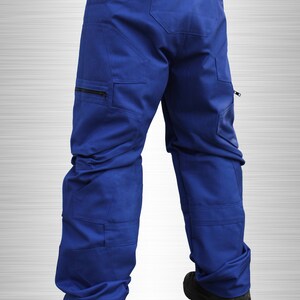 May include: Royal blue work trousers with multiple pockets and a zip closure. The trousers have a structured design and are worn with black work boots. The image is set against a silver gradient background.