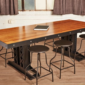 May include: A long wooden table with a black metal frame and four black metal stools. The table has a natural wood finish and the stools have a black metal frame and a black leather seat.