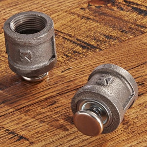 May include: Two metal pipe fittings with a silver knob on one. The fittings are gray and have a textured surface. The fittings are on a wooden surface.