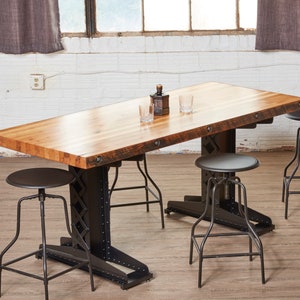 May include: A long wooden table with a distressed finish and black metal legs. The table is surrounded by four black metal stools with round seats.
