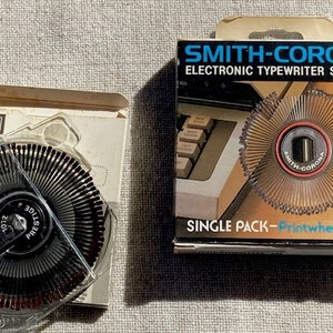 May include: A single pack of Smith-Corona Printwheel for electronic typewriters. The package is white with blue and red text. The printwheel is silver with a red and black center. The printwheel is labeled "Smith-Corona".