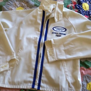 May include: White jacket with blue stripes down the front and a blue embroidered logo that says "WT World Tribune Press" on the left side.