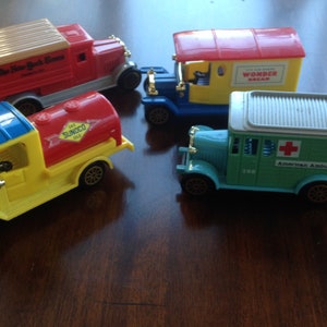 Puede incluir: Cuatro camiones de juguete vintage, incluyendo un camión de reparto rojo del New York Times, un camión de gasolina amarillo Sunoco, un camión de reparto azul y amarillo Wonder Bread y un camión de ambulancia americano verde.
