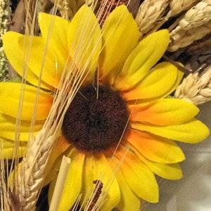 Pu&ograve; includere: Un girasole giallo con un centro marrone &egrave; circondato da steli di grano e altri elementi floreali secchi.