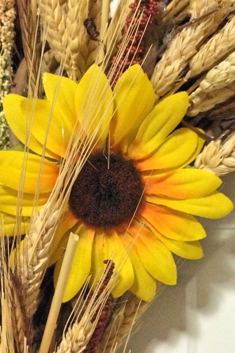 Pu&ograve; includere: Un girasole giallo con un centro marrone &egrave; circondato da steli di grano e altri elementi floreali secchi.