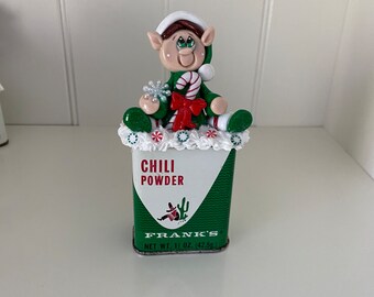 Polymer Clay Elf sitting on a Vintage Spice Tin with a Candy Cane and Peppermint Swirls