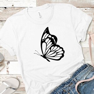 May include: A white t-shirt with a black butterfly graphic design. The butterfly is in flight with its wings spread out.
