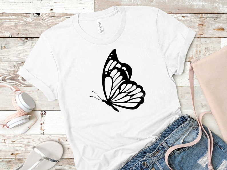 May include: A white t-shirt with a black butterfly graphic design. The butterfly is in flight with its wings spread out.