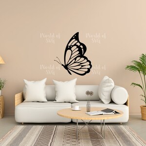 May include: A white couch with two pillows and a coffee table in front of it. A black butterfly silhouette is on the wall behind the couch. The wall is a light beige color. There is a potted plant in the corner of the room.