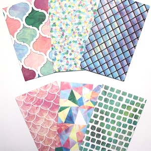 Puede incluir: Seis sobres rectangulares con patrones distintos: un diseño de cuatrifolio multicolor, un estampado de confeti vibrante, una cuadrícula iridiscente oscura, un patrón de escamas de pez con textura de mármol rosa, un estampado geométrico triangular y una cuadrícula verde.