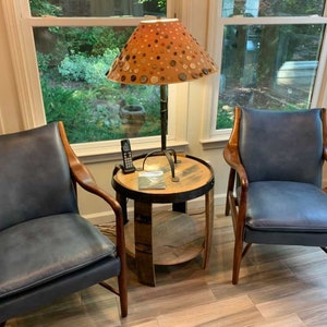 May include: Two blue leather chairs with wooden frames and a wooden side table with a lamp with a patterned lampshade. The lampshade is made of fabric and has a pattern of buttons.