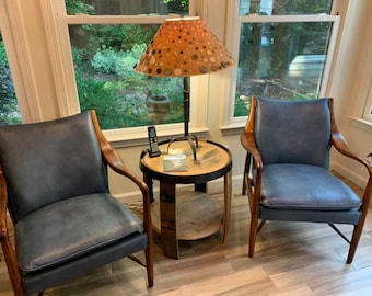 May include: Two blue leather chairs with wooden frames and a wooden side table with a lamp with a patterned lampshade. The lampshade is made of fabric and has a pattern of buttons.