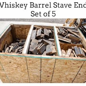 May include: A set of five whiskey barrel stave ends, stacked in a wooden crate. The ends are made of dark wood and have a rustic appearance. The crate is made of plywood and has a green trim.