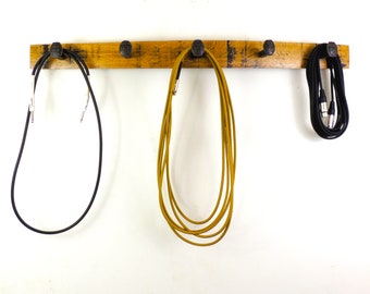 May include: A wooden wall-mounted rack with five metal hooks, used to hang three different colored cords.