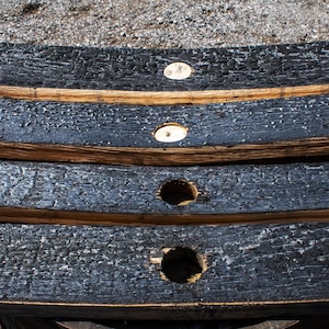 May include: Three curved wooden barrel staves with a charred black exterior finish. Each stave features a circular hole drilled through the center, revealing the natural light brown wood grain underneath the burnt surface texture.