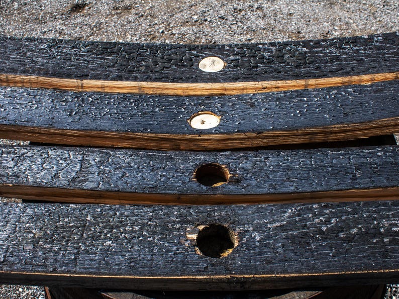 May include: Three curved wooden barrel staves with a charred black exterior finish. Each stave features a circular hole drilled through the center, revealing the natural light brown wood grain underneath the burnt surface texture.